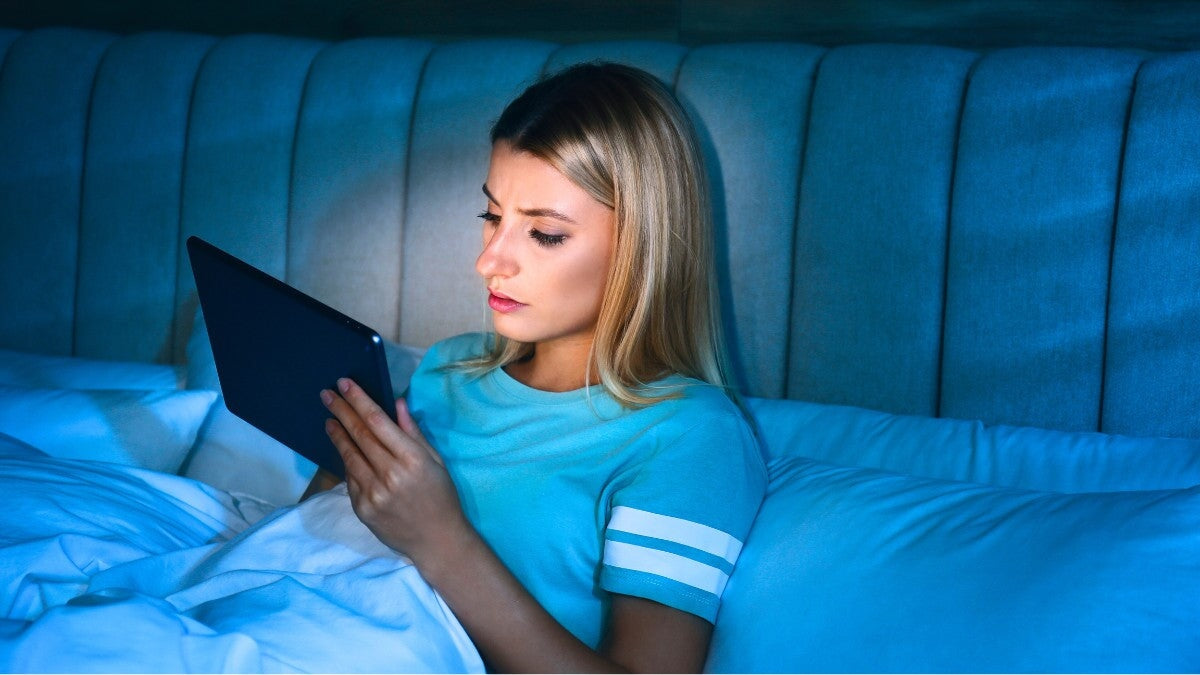 Jeune femme utilisant une tablette au lit la nuit.