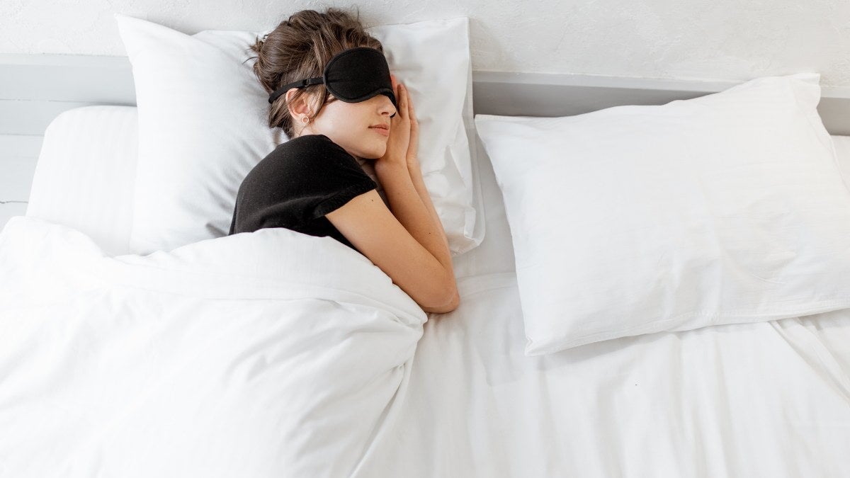 une femme qui dort dans son lit en portant un masque pour les yeux