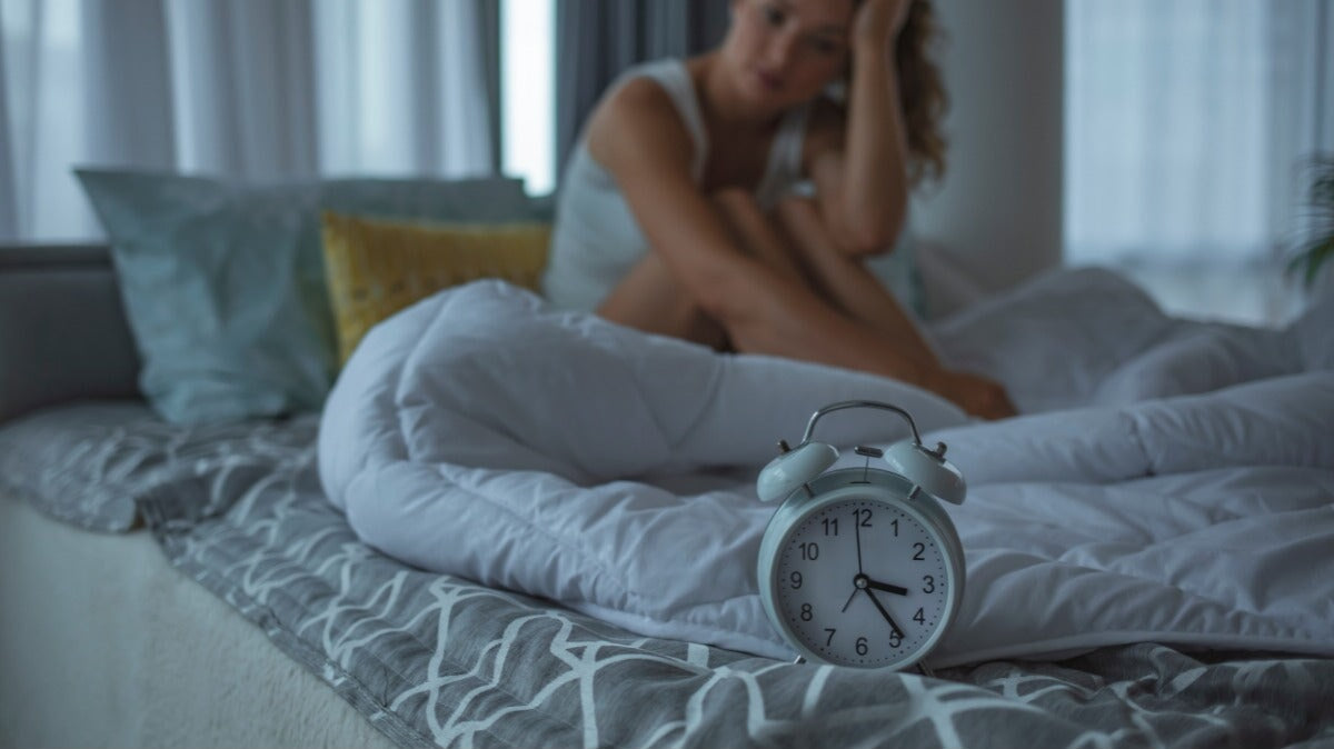 une femme souffrant d'insomnie assise sur son lit avec une horloge à côté d'elle