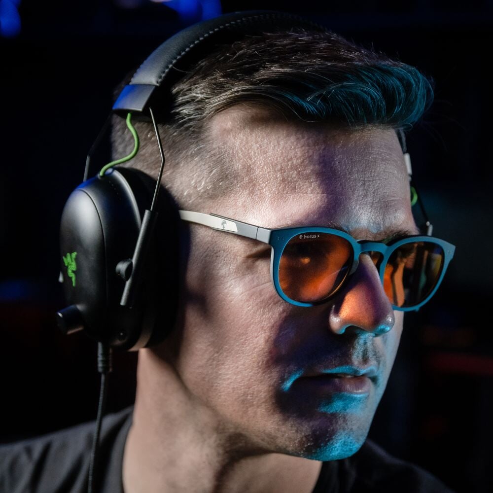 Notre cofondateur Matthieu porte les lunettes gamer urban revolution avec verre ambré et un casque audio sur fond noir de profil
