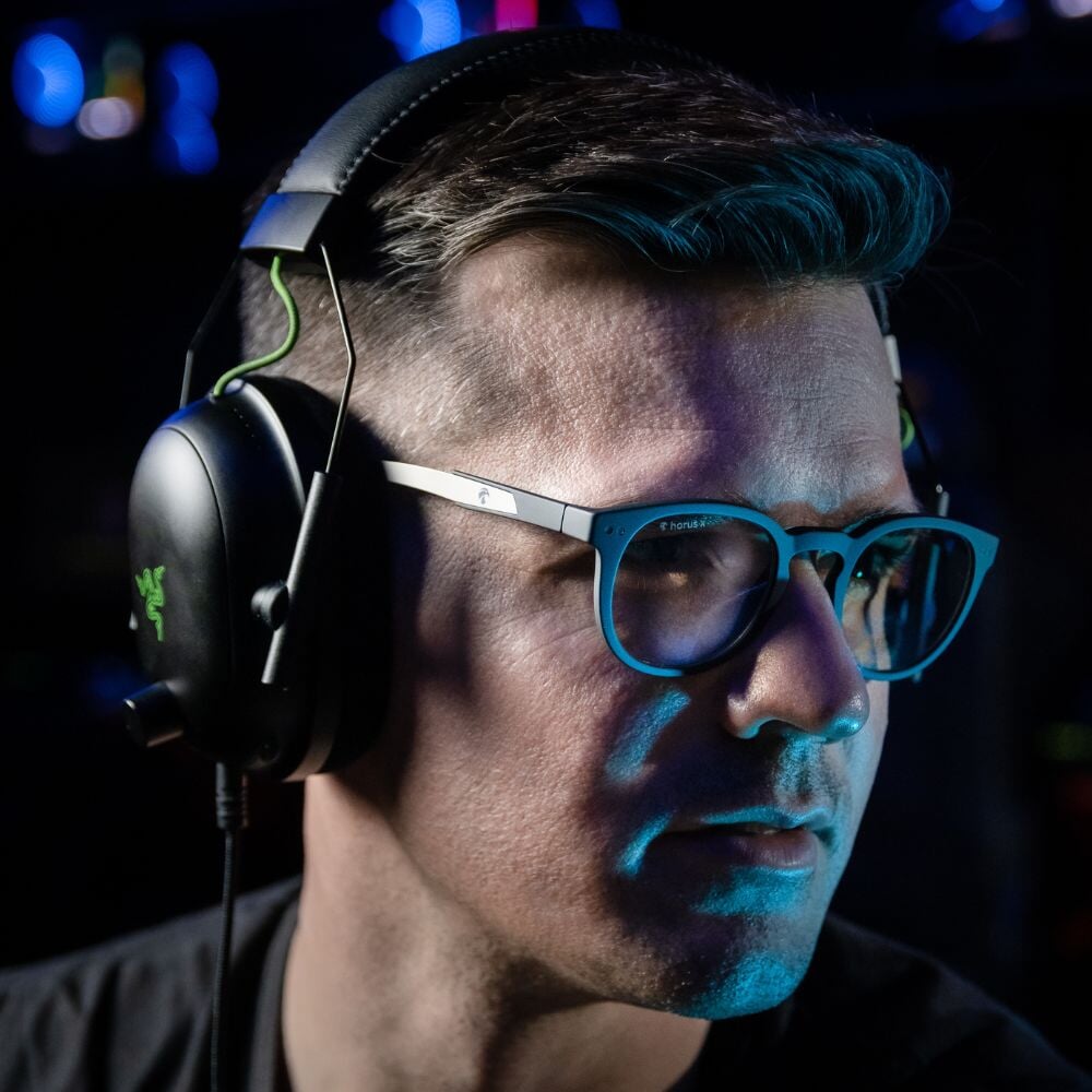 Notre cofondateur Matthieu porte les lunettes gamer urban revolution avec verre clair et un casque audio sur fond noir de profil